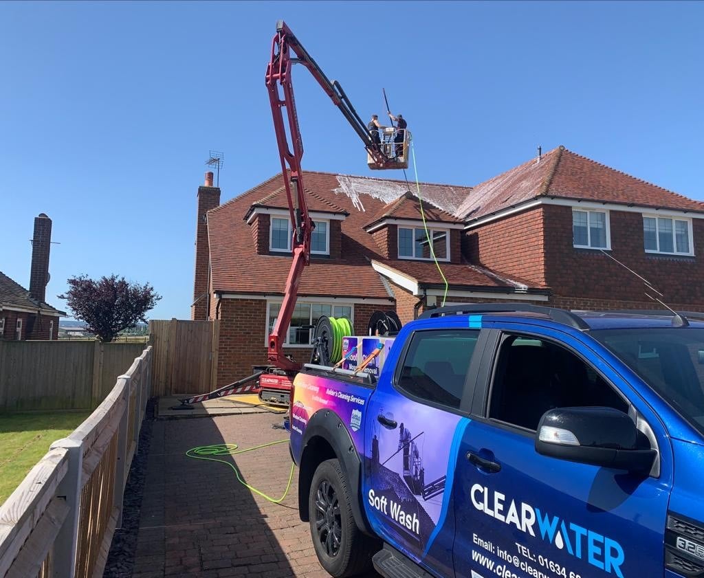 Workers using a cherry picker to clean a residential roof, with a Clearwater branded vehicle parked nearby, showcasing professional cleaning services in Kent.