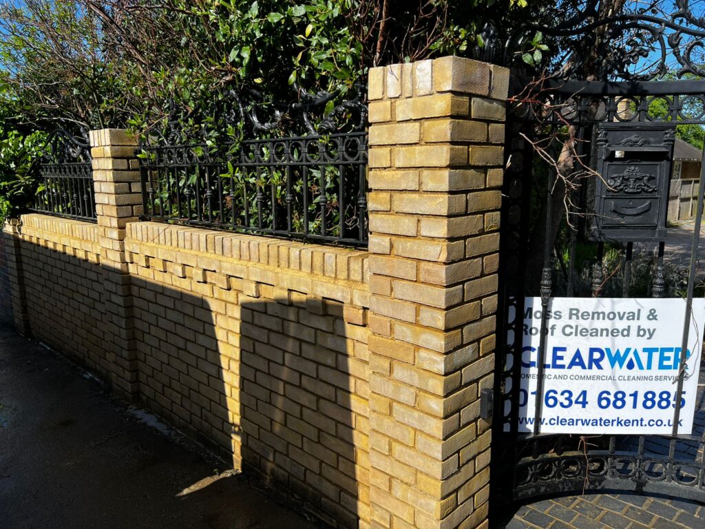 Brick wall and gate with greenery, featuring a Clearwater Cleaning Services advertisement for moss removal and roof cleaning, highlighting professional cleaning solutions for patios and driveways in Kent.