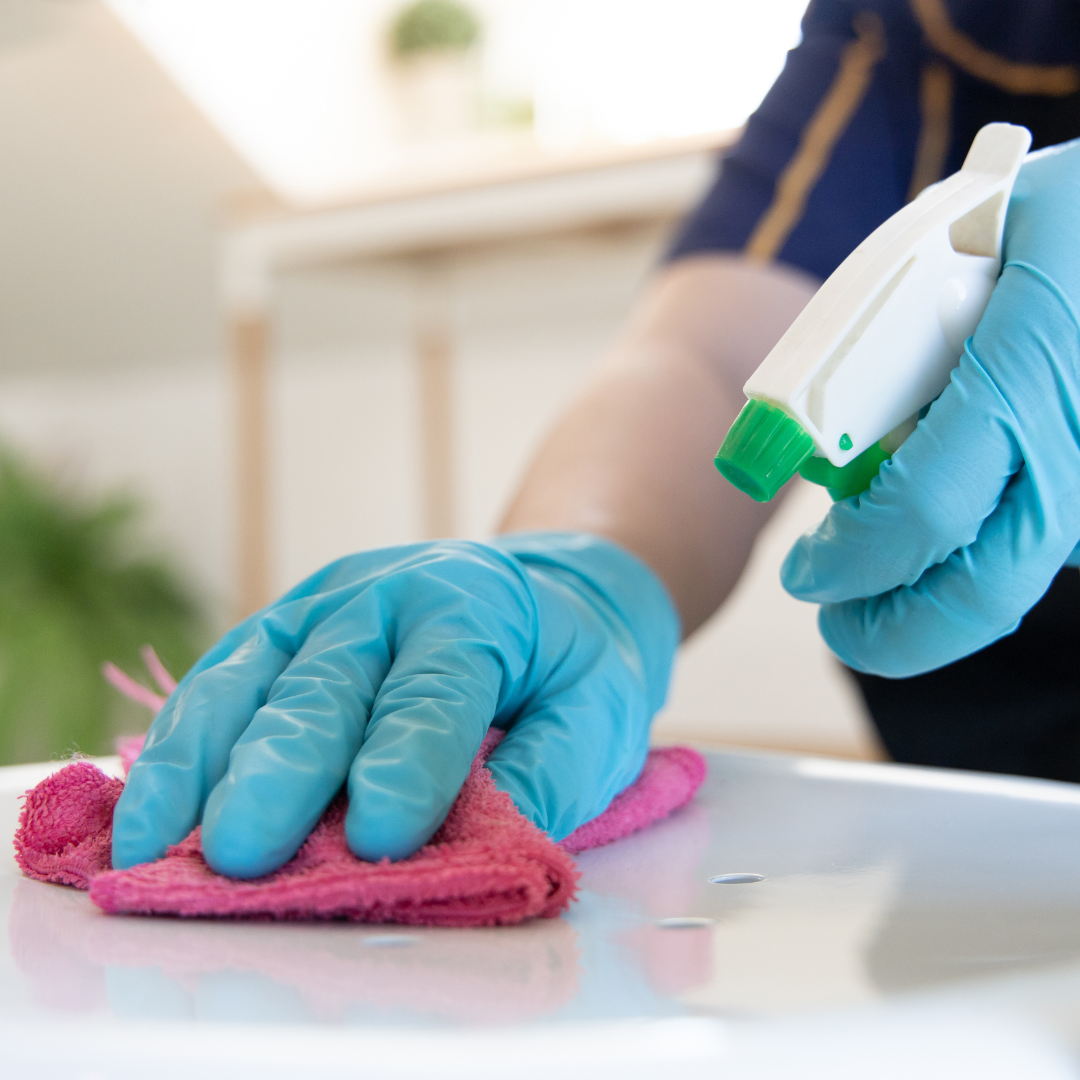 Person wearing blue gloves cleaning a surface with a pink cloth and spray bottle, illustrating professional cleaning services offered by Clearwater Kent.