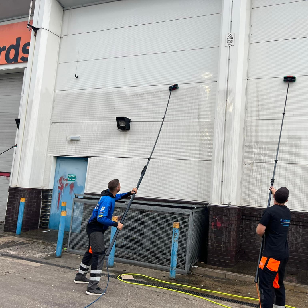 Two workers using extendable poles to clean the exterior of a building, showcasing professional cleaning services in action.