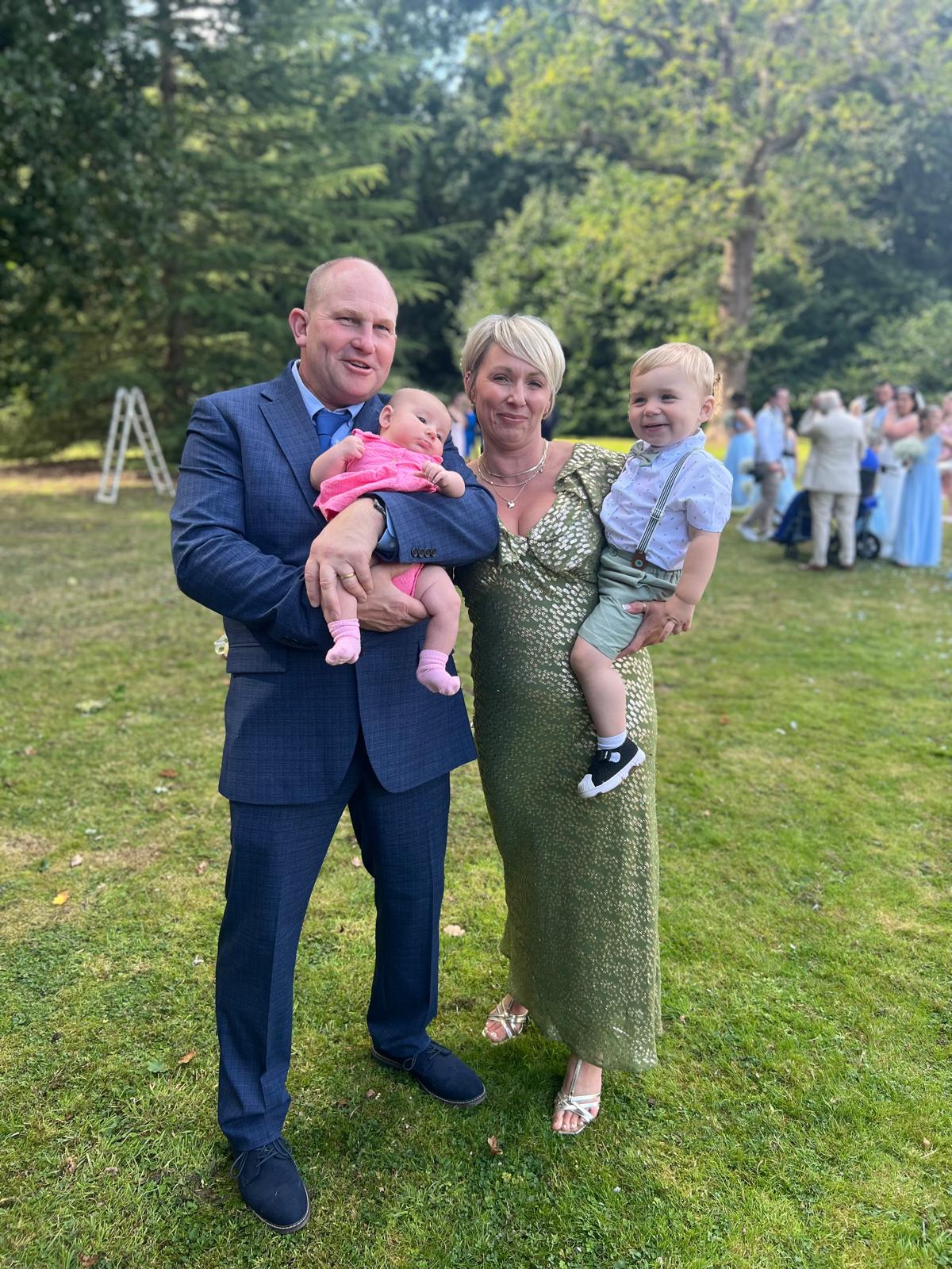 Family portrait featuring a couple holding two young children in a garden setting, showcasing a sense of togetherness and warmth, reflecting Clearwater Kent's family-run cleaning business ethos.